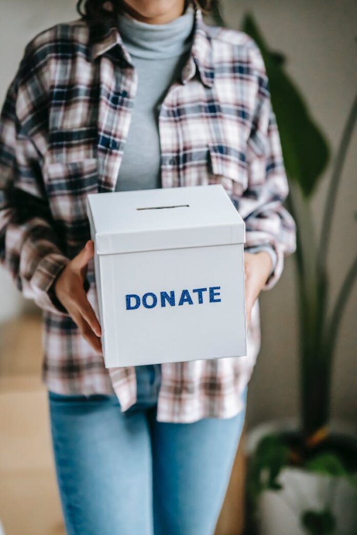Crop unrecognizable woman in casual clothes standing with box for donations in hands on light room