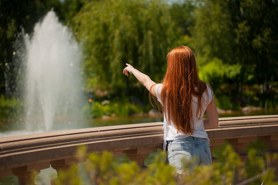 Shallow Focus Photo of Woman Standing in Front of Body of Water With Fountain